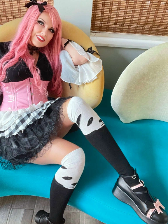 A person with pink hair and a corset dress lounging on a chair with playful panda-themed knee-high socks.