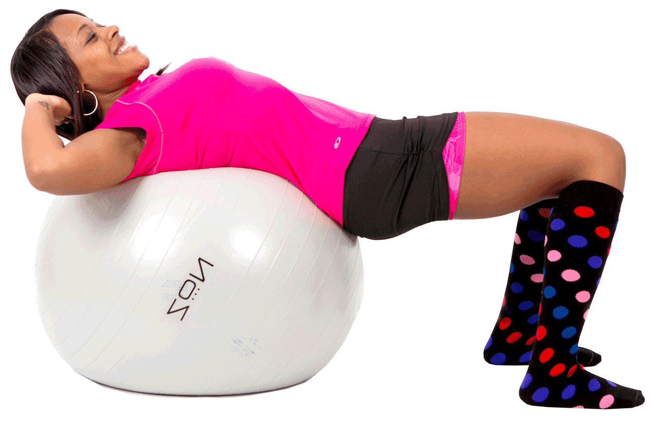 A joyful woman exercising on a fitness ball, wearing a vibrant pink top, black shorts, and knee-high socks patterned with colorful polka dots