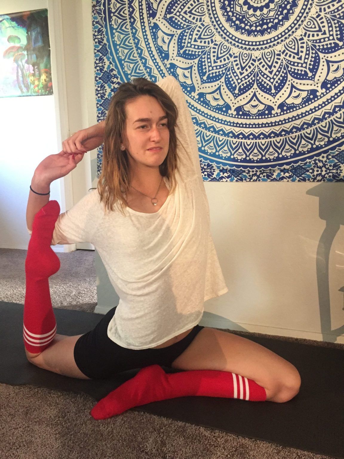 girl holding a yoga pose at home on yoga mat wearing black shorts, white top and red tube socks