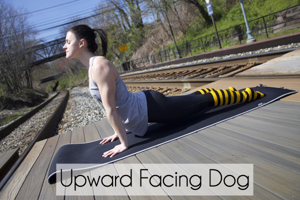 woman practicing upward facing dog pose on a yoga mat alongside railroad tracks wearing leggings, striped socks and tank top